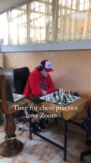 Joshua wearing headphones and ball cap seated at a chess board.