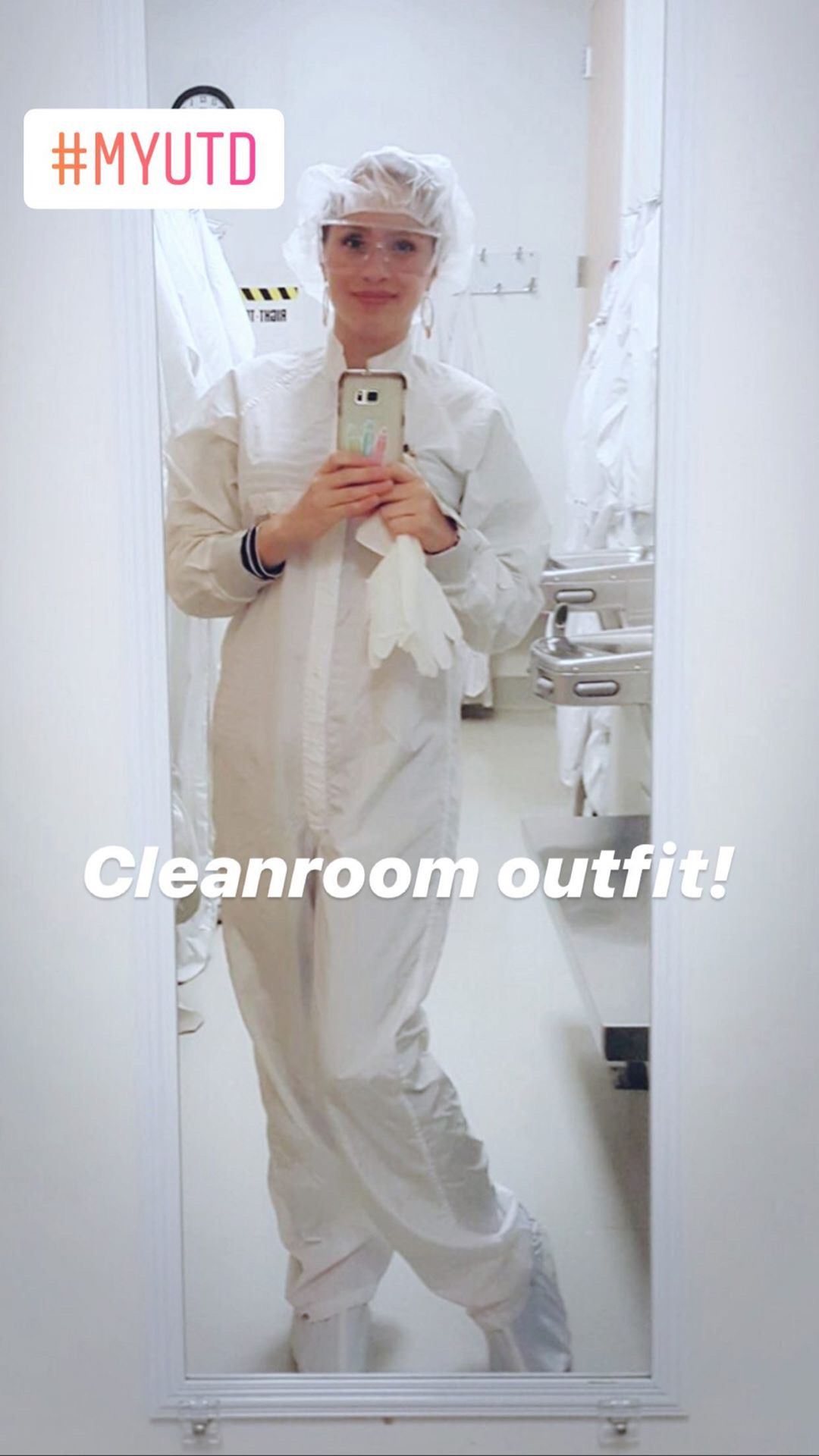 Patty is wearing a white jumpsuit, bonnet and shoe covers, and goggles. She's taking a selfie in a mirror.