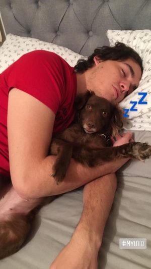 Joshua appears asleep in bed with a dog. 