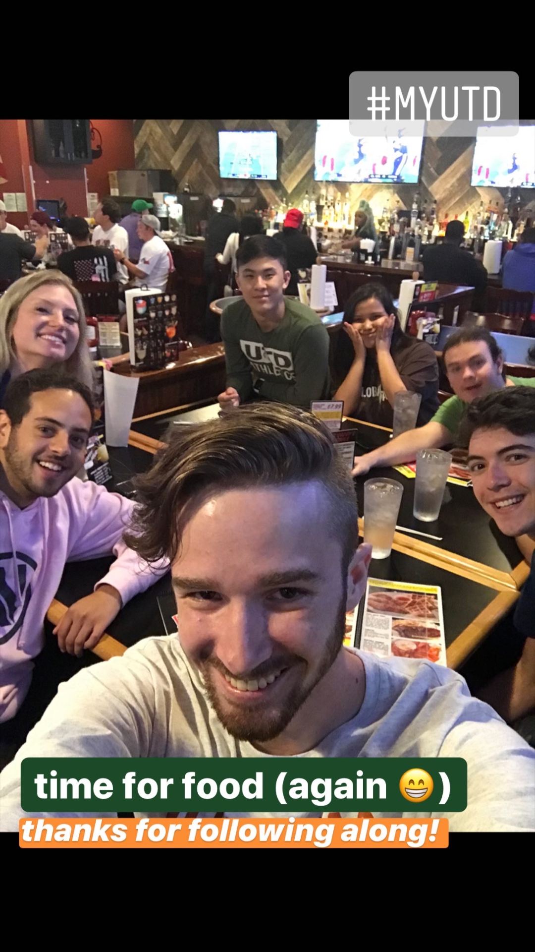  Garrett taking a selfie in a restaurant with a group of friends behind him.