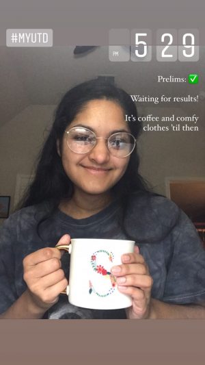 Sherin holding a white coffee mug featuring a gold handle and flower illustration of the letter S. 