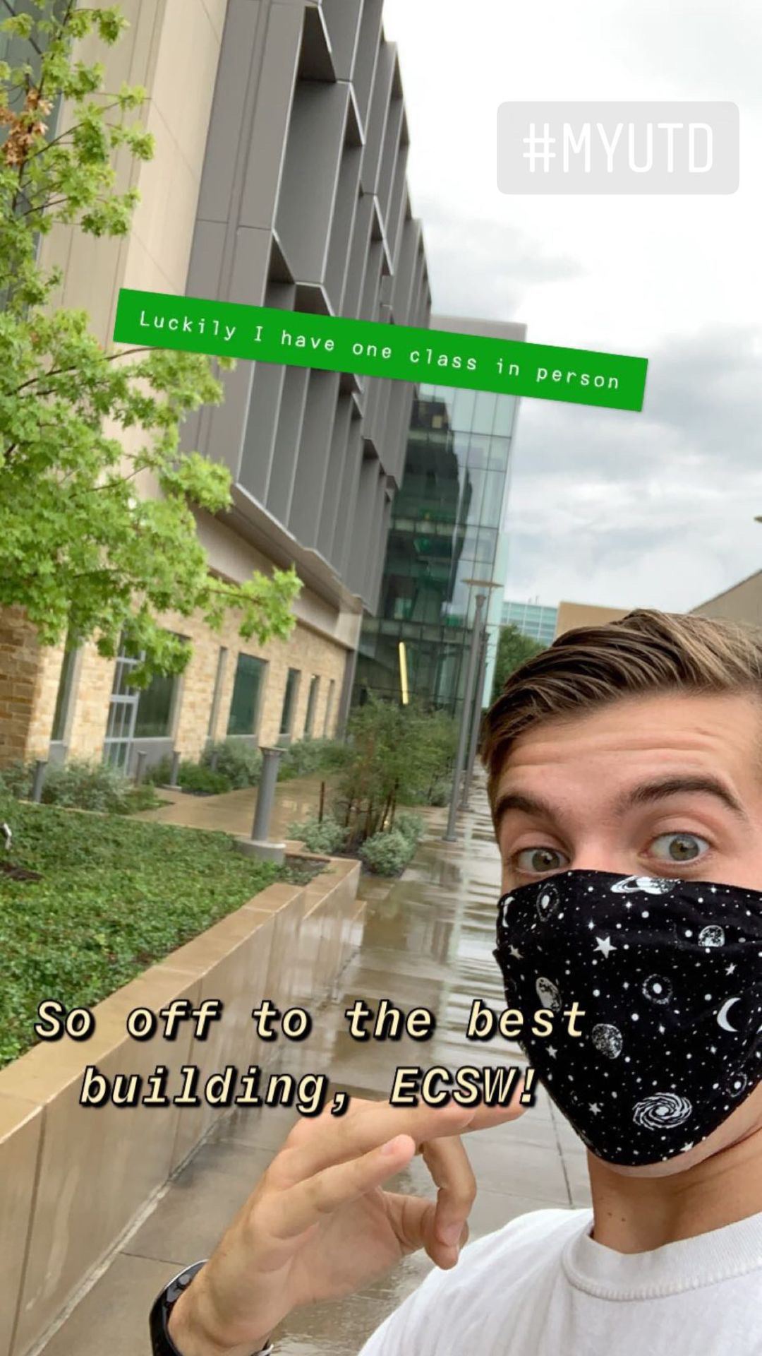 A Trent selfie. A campus building and wet sidewalk is behind him. He's doing a mini whoosh hand sign.