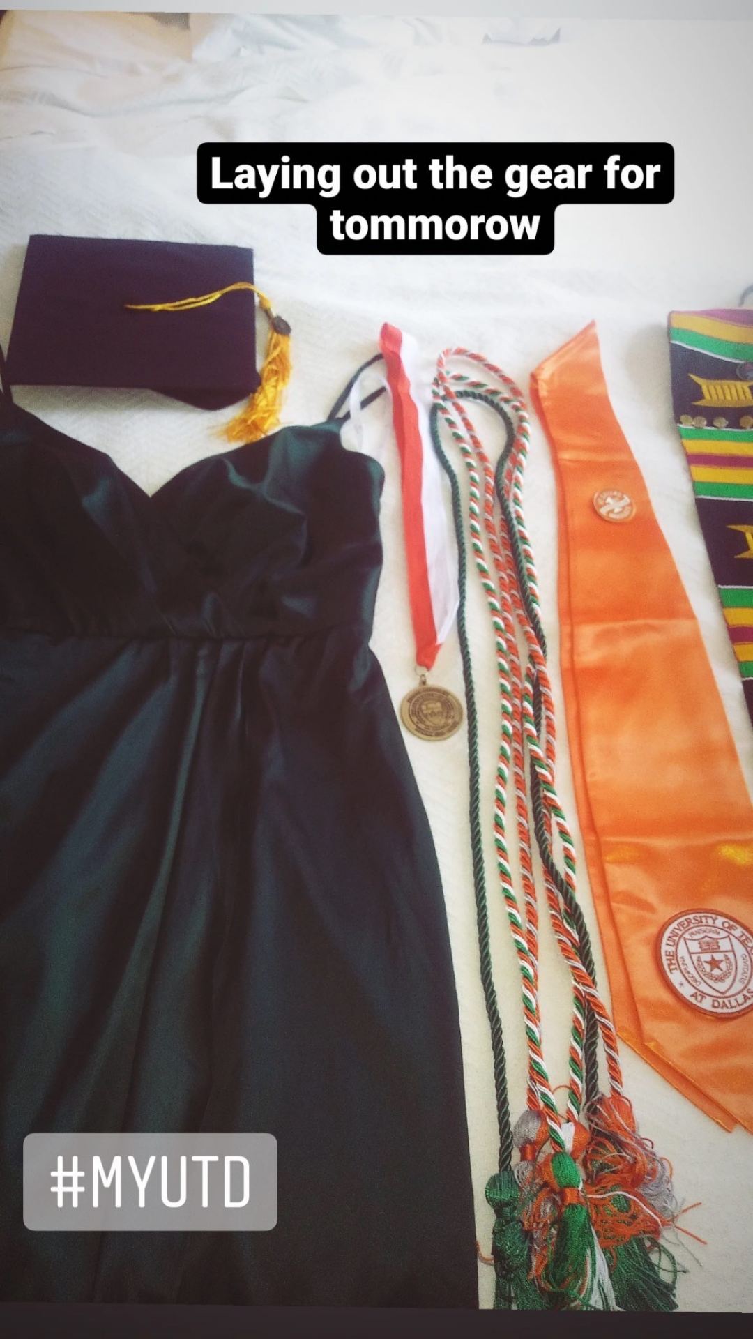 A black dress, graduation cap, and colorful sashes laid out.