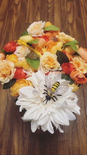 A bunch of yellow, red and orange flowers, plus a large white flower with a bee figurine on it. This may be the decoration of Morganne's graduation cap.