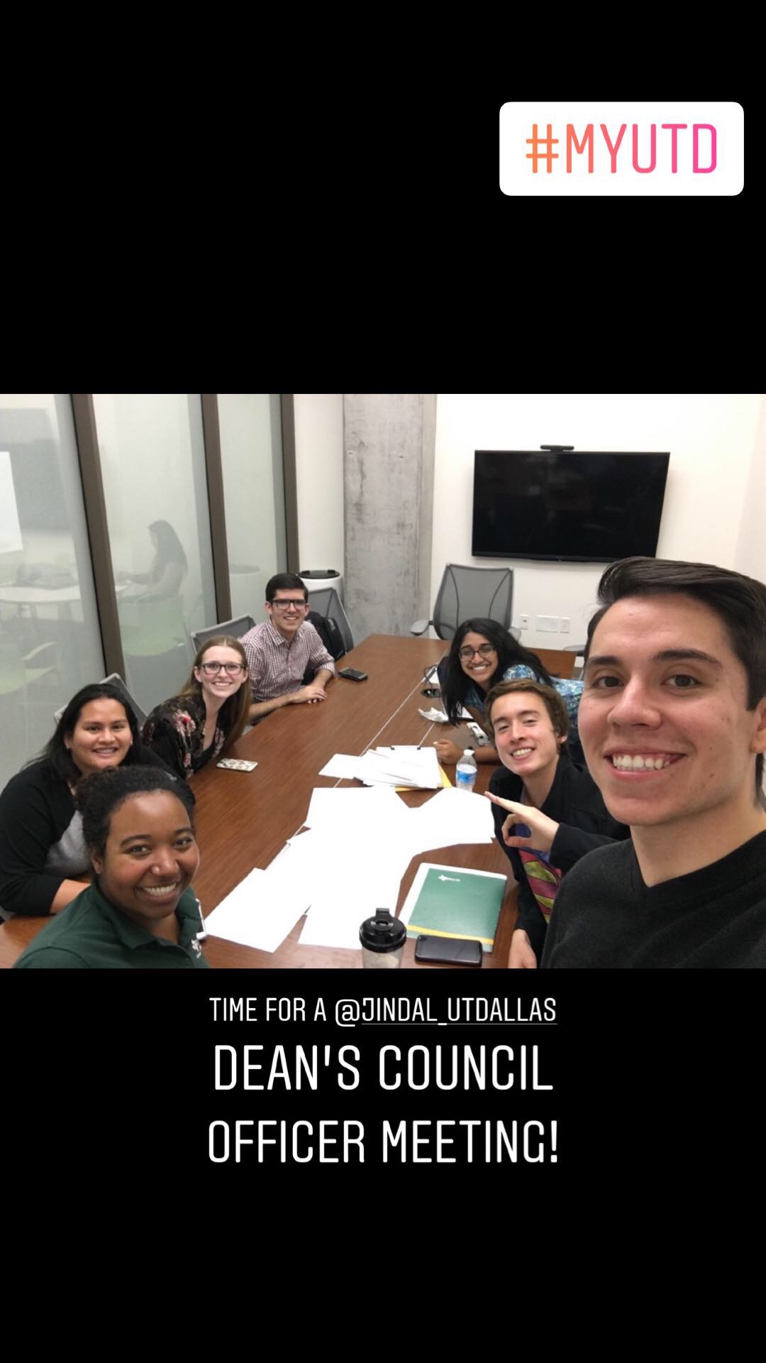 Charlie and six others take a group selfie while seated around a conference table.