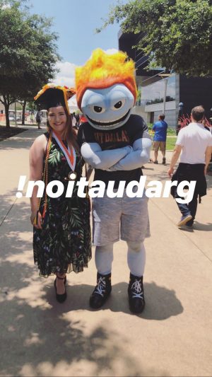 Morganne, wearing graduation cap and medal, poses with Temoc outdoors on campus.