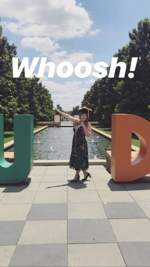 Morganne stands and does a whoosh sign between giant letters U and D on the campus mall. 