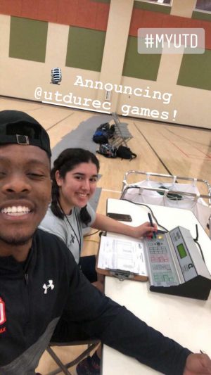 Xavier and another student at a table on a basketball court. There's an electronic control board in front of them. Microphone emoji.